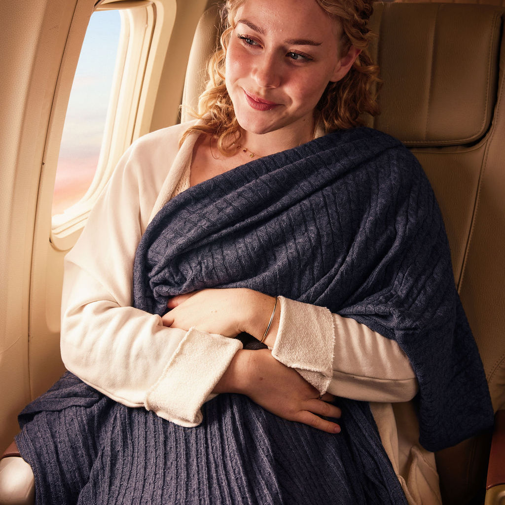 Cozy navy blue blanket in travel setting, made from soft material, ideal for comfort on flights.