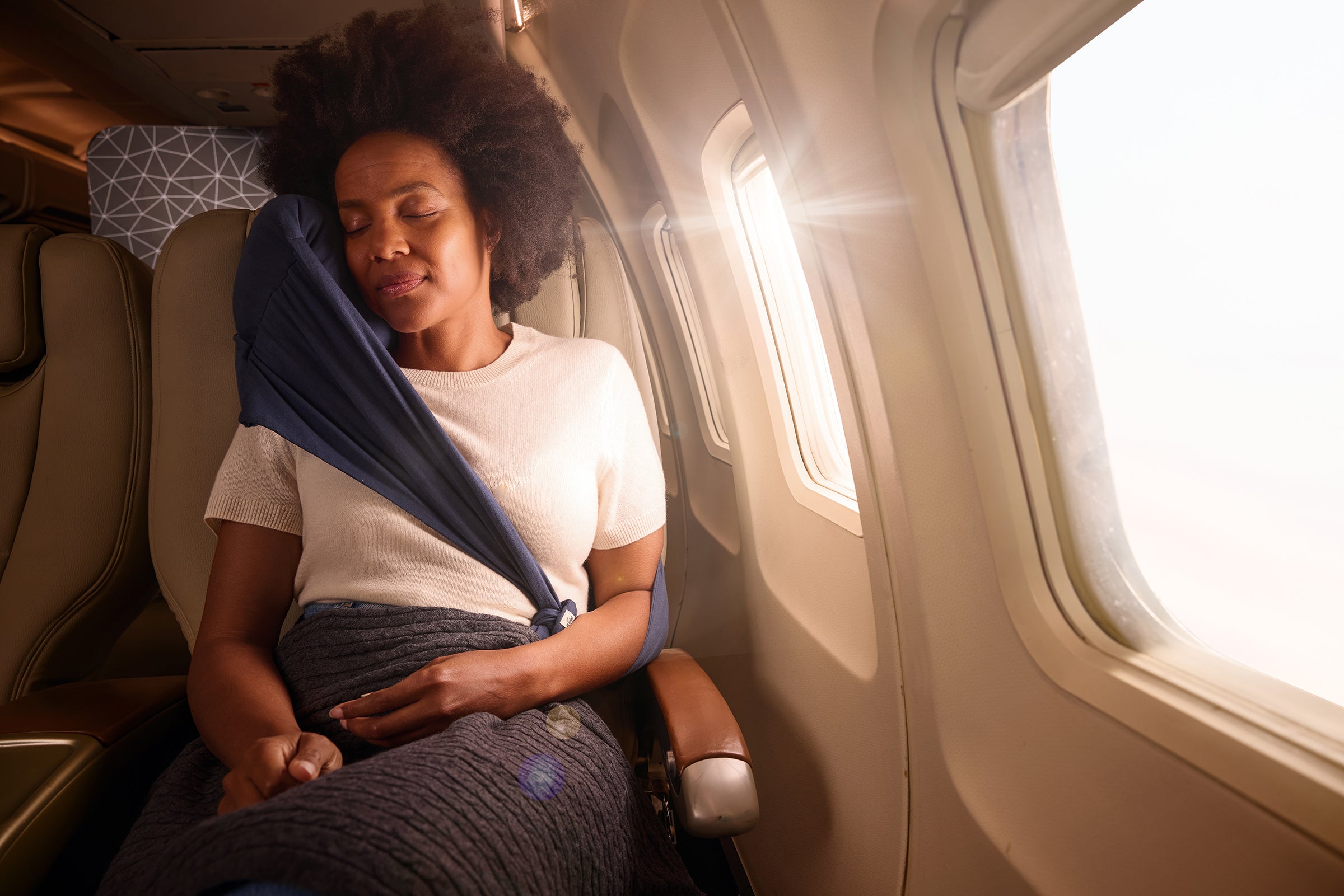 Comfortable travel scene with a woman sleeping in a cozy blanket on an airplane.